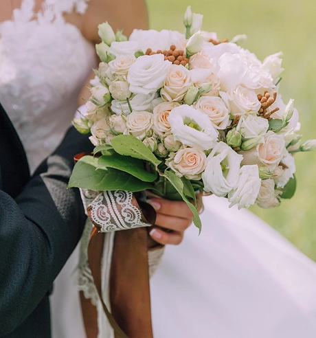 Een bruid met een boeket witte rozen en bloemen, waarbij de nadruk ligt op elegante bruiloftsdetails en een romantisch bloemstuk.