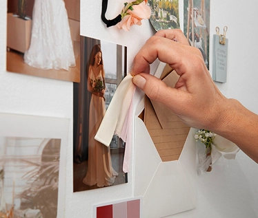 Iemand die met de hand een stofstaal op een moodboard voor een bruiloft legt, samen met foto’s en inspiratiebronnen, ter illustratie van ideeën voor evenementenplanning en styling.