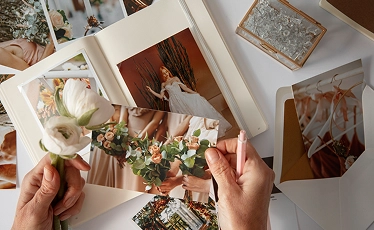 Handen die gedrukte trouwfoto’s en albumpagina’s ordenen, waarmee de vastgelegde herinneringen en het verhaal van de trouwdag tot leven komen.
